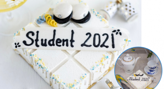 Vit studenttårta dekorerad med studentmössor och gult och blått strössel på uppdukat bord